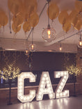 Load image into Gallery viewer, Decorative setup with yellow balloons, hanging lights, and illuminated 'CAZ' letters.