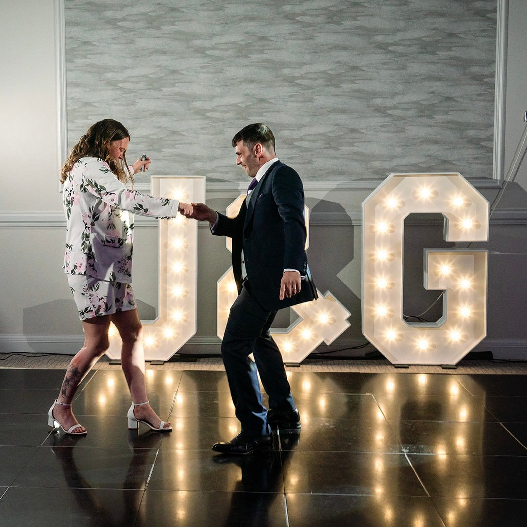 Couple dancing in front of glowing light up initials J & G, adding a fun and personal element to their wedding celebration.