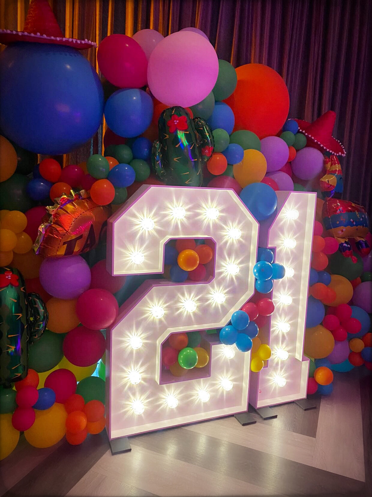 Brightly lit big 21 light up numbers surrounded by colourful balloon display for birthday party celebration