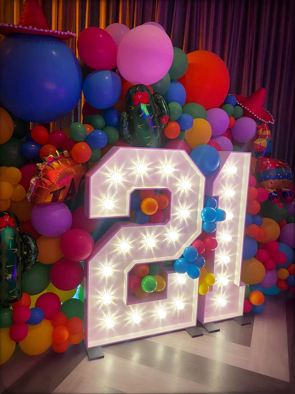 Brightly lit big 21 light up numbers surrounded by colourful balloon display for birthday party celebration