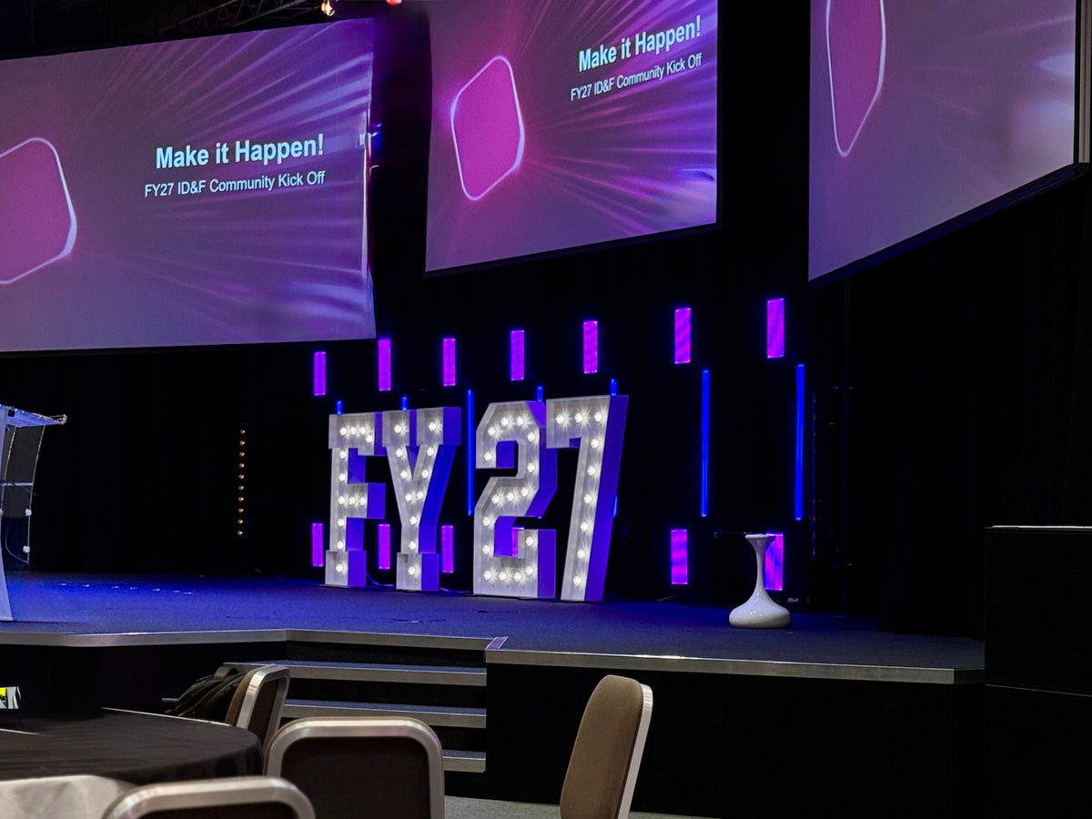 Large light up letters spelling FY27 at a corporate kick-off event with balloons and attendees in the background