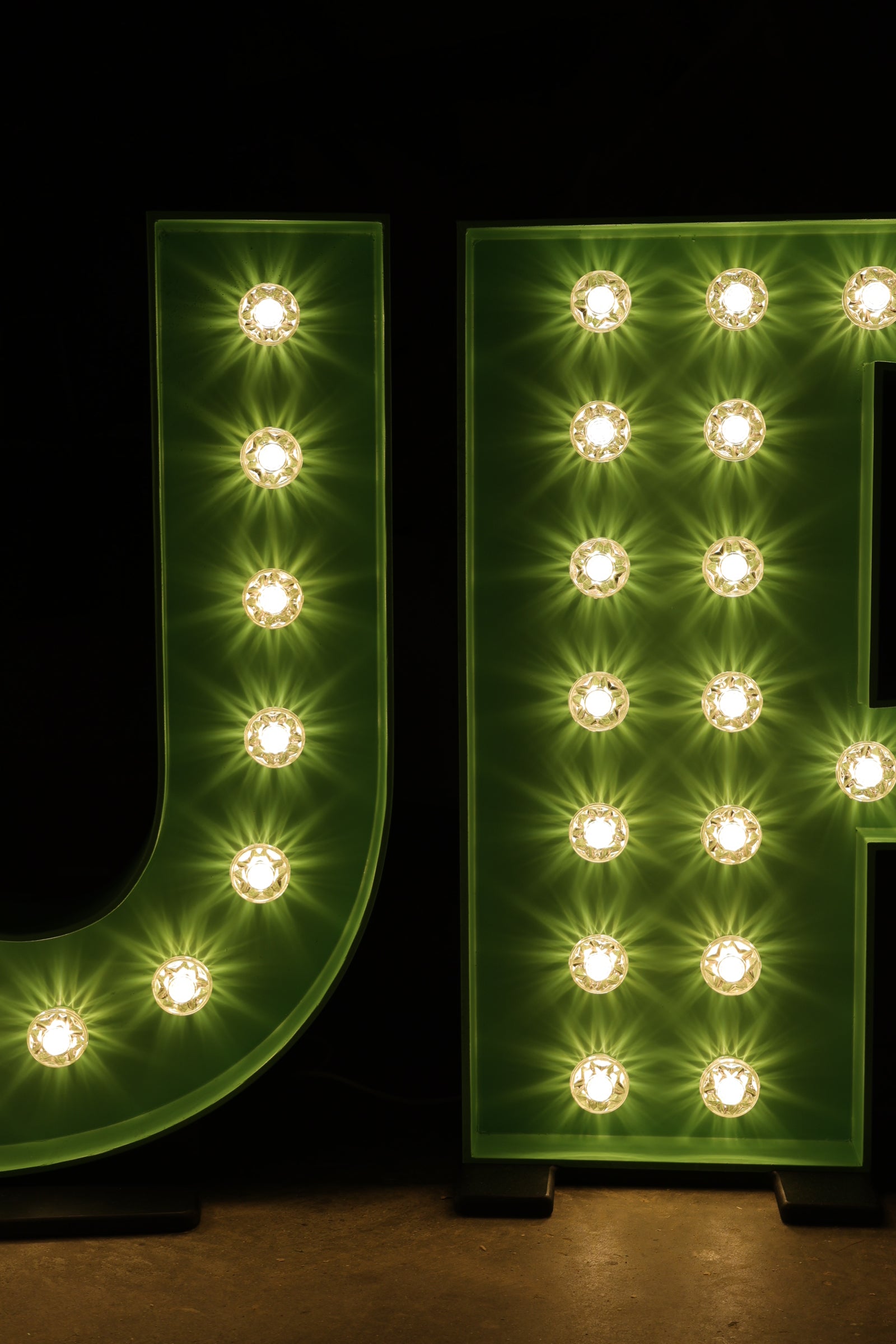 Green illuminated letter with a marquee light effect on a dark background -