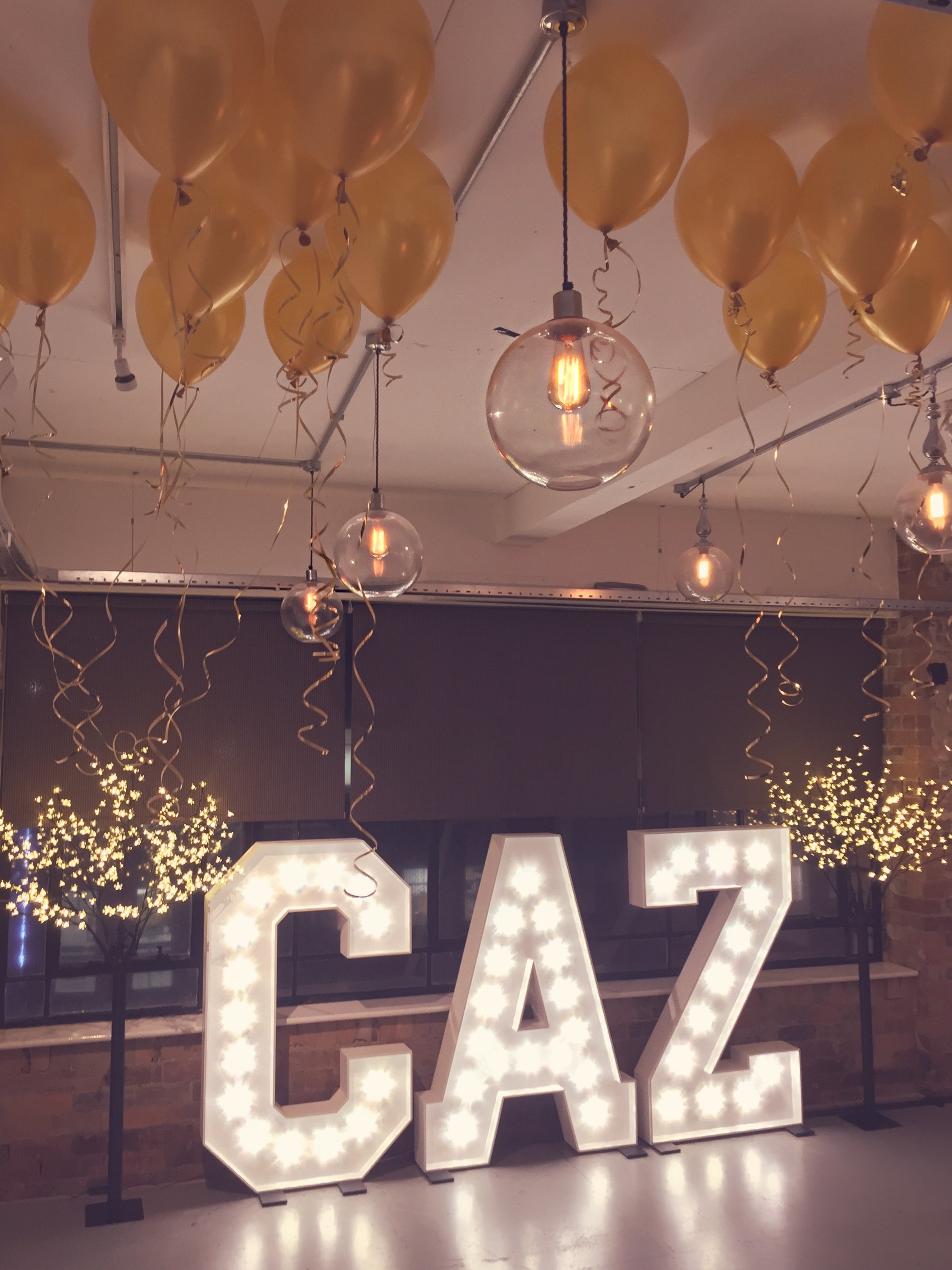 Decorative setup with yellow balloons, hanging lights, and illuminated 'CAZ' letters.