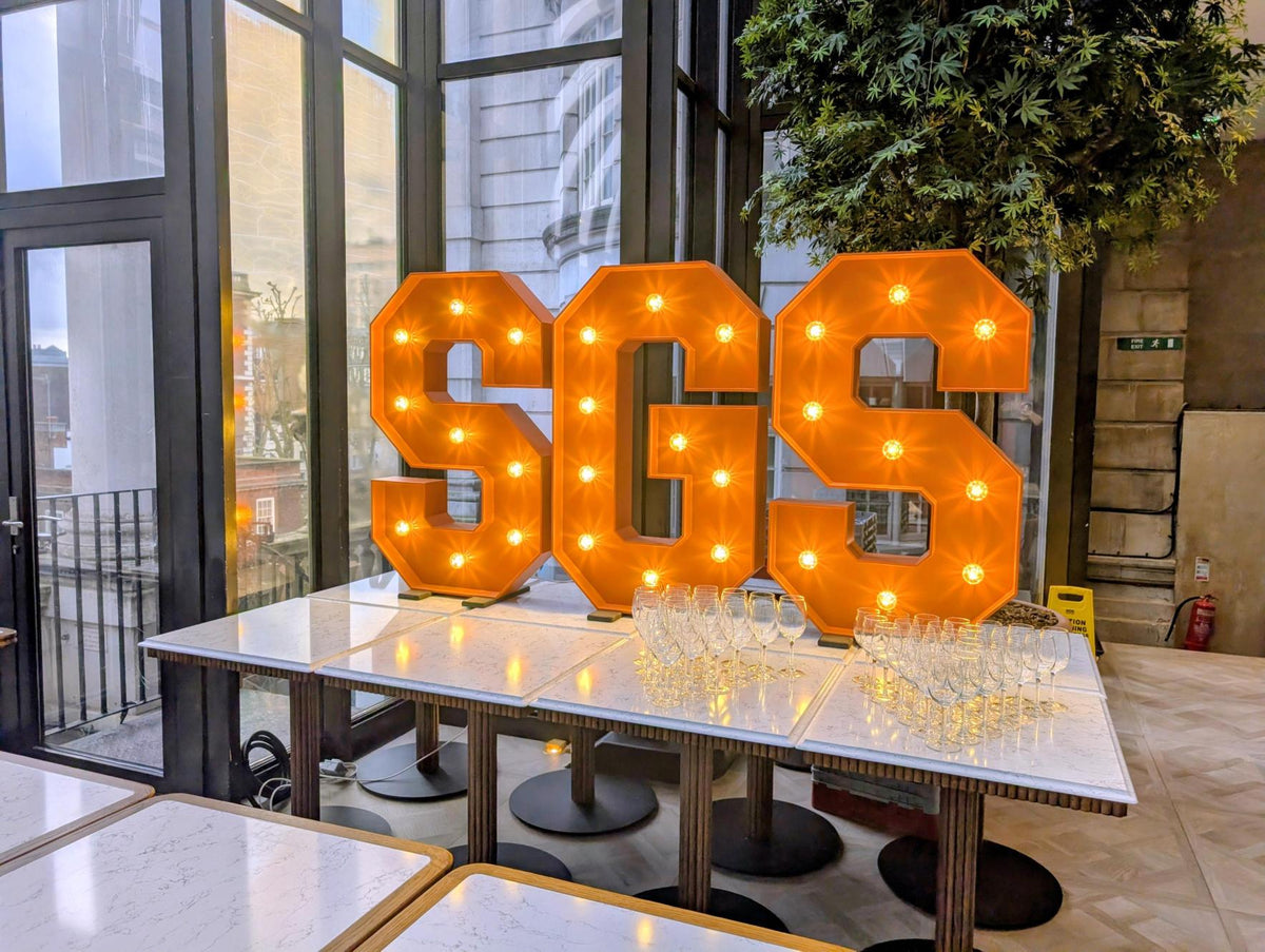 Decorative letters 'SGS' on a table with glasses in an indoor setting.