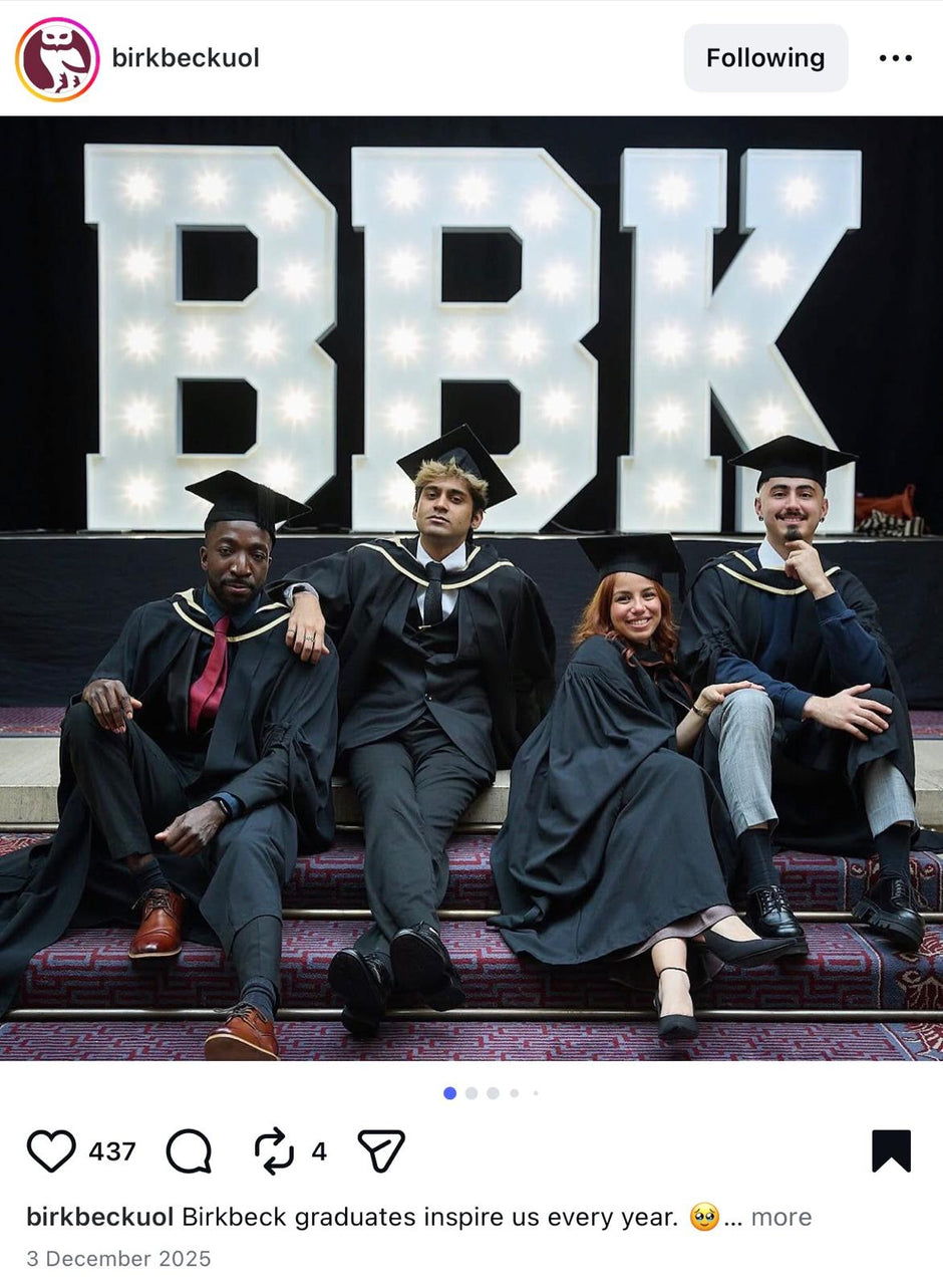 Graduates in academic dress sitting on steps with 'BBK' illuminated behind them, likely at Birkbeck University of London.