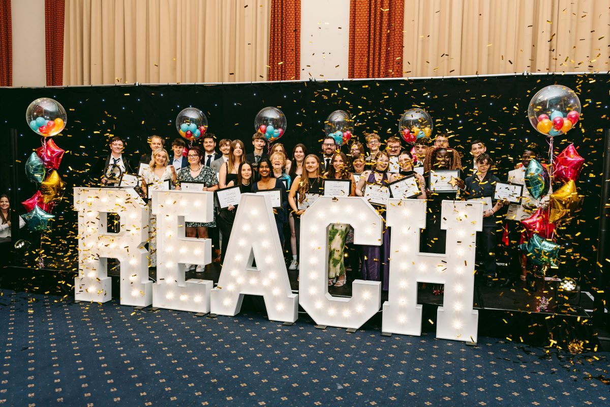 Large light up letters spelling REACH at a student awards ceremony with confetti and group celebration