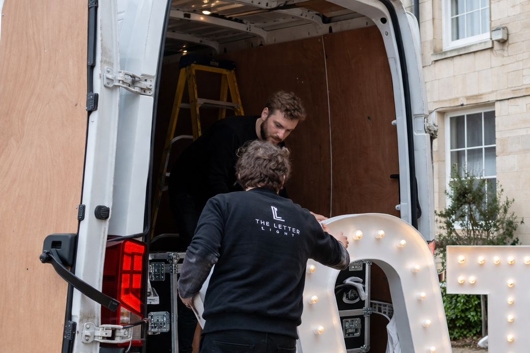 Two men loading a van with a large 'OTM' sign in the foreground.