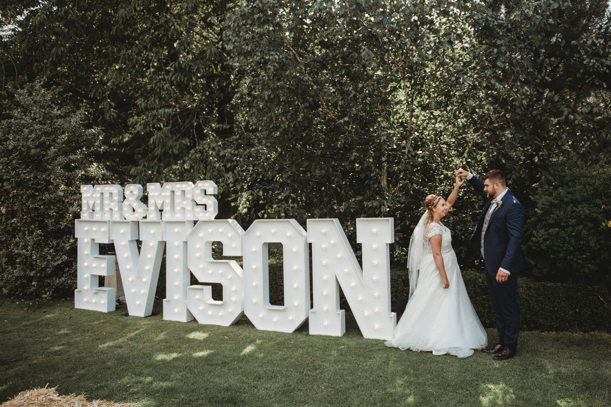 Light up MR & MRS EVISON letters at an outdoor wedding with bride and groom dancing in garden setting